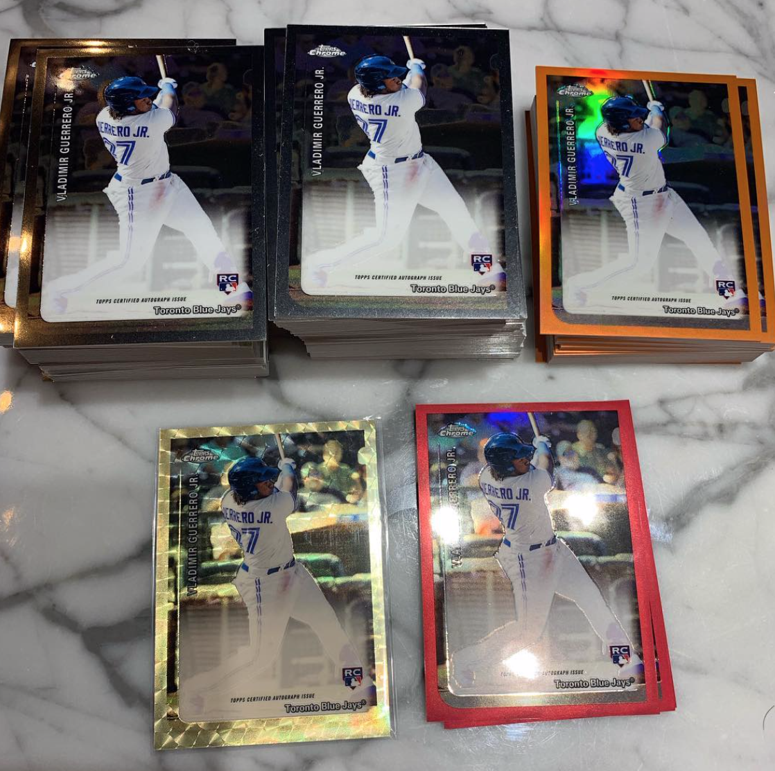 Stacks of Vlad Jr. sports cards (2019 Topps Chrome - Rookie Variation Auto (Possible 20th Anniversary Insert Auto?) & Dual Autos) on a marble countertop